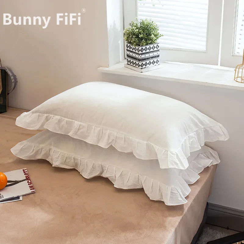 A set of two white washed cotton pillowcases with ruffled edges displayed on a wooden surface.