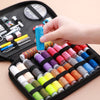 A hand is holding a spool of bright blue thread inside a black sewing kit containing various threads and tools.