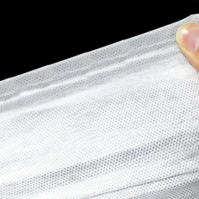 A close-up view of a white disposable non-woven beauty and salon sheet being held by a finger.