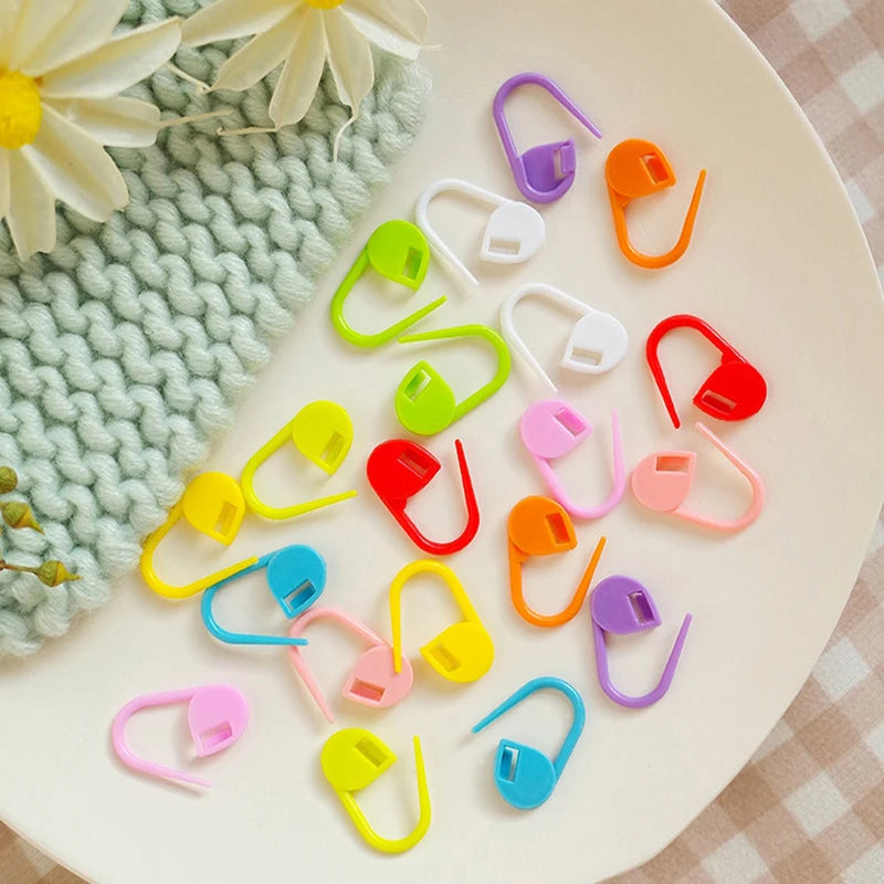 A collection of colorful stitch markers in various shapes and colors scattered on a white surface.