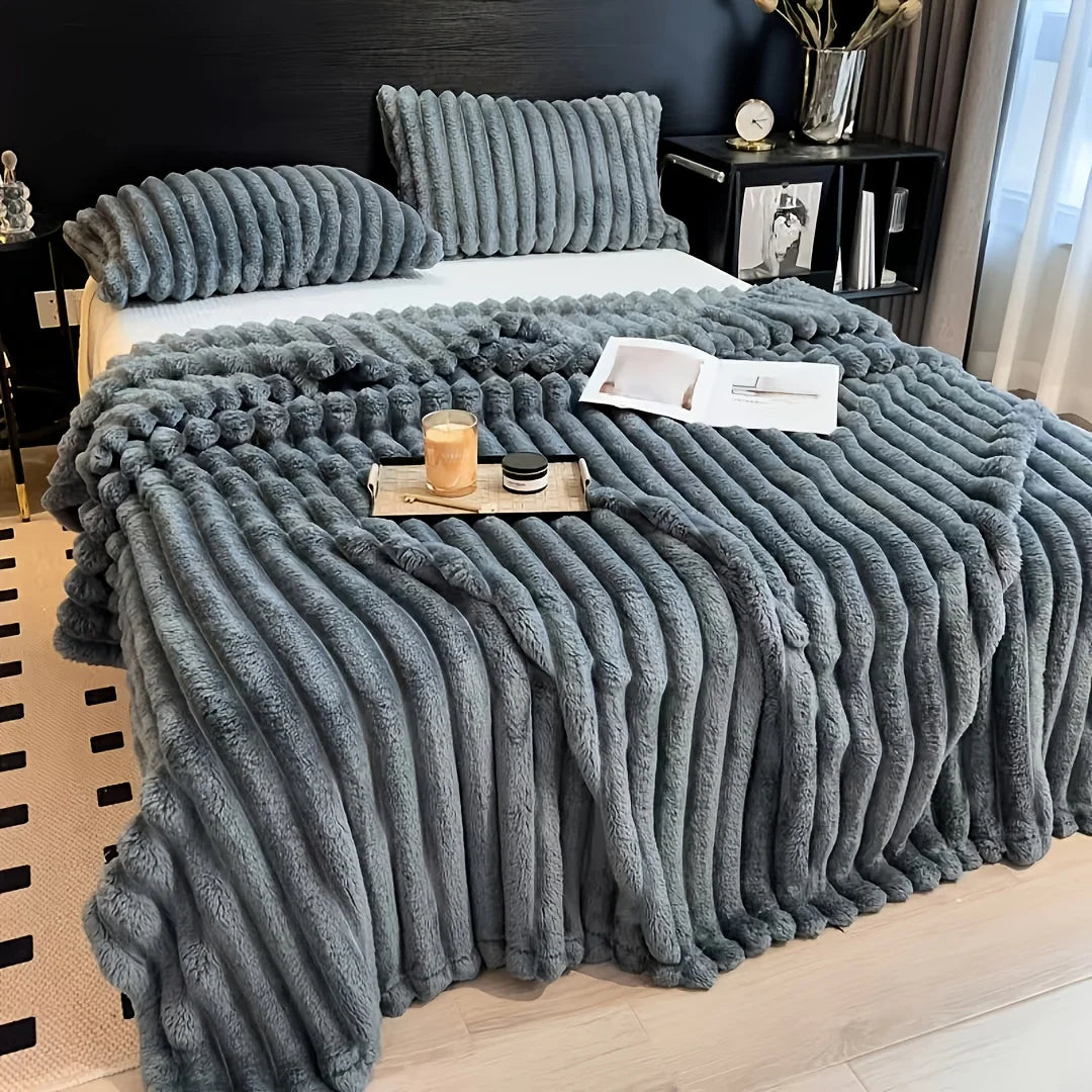 A thick gray knitted blanket with vertical stripes is draped over a bed, featuring natural wood accents.
