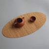 A terracotta teapot and cup resting on a round, woven bamboo tea mat.