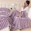 A fluffy purple fleece throw blanket draped over a white bed, being held by a person.