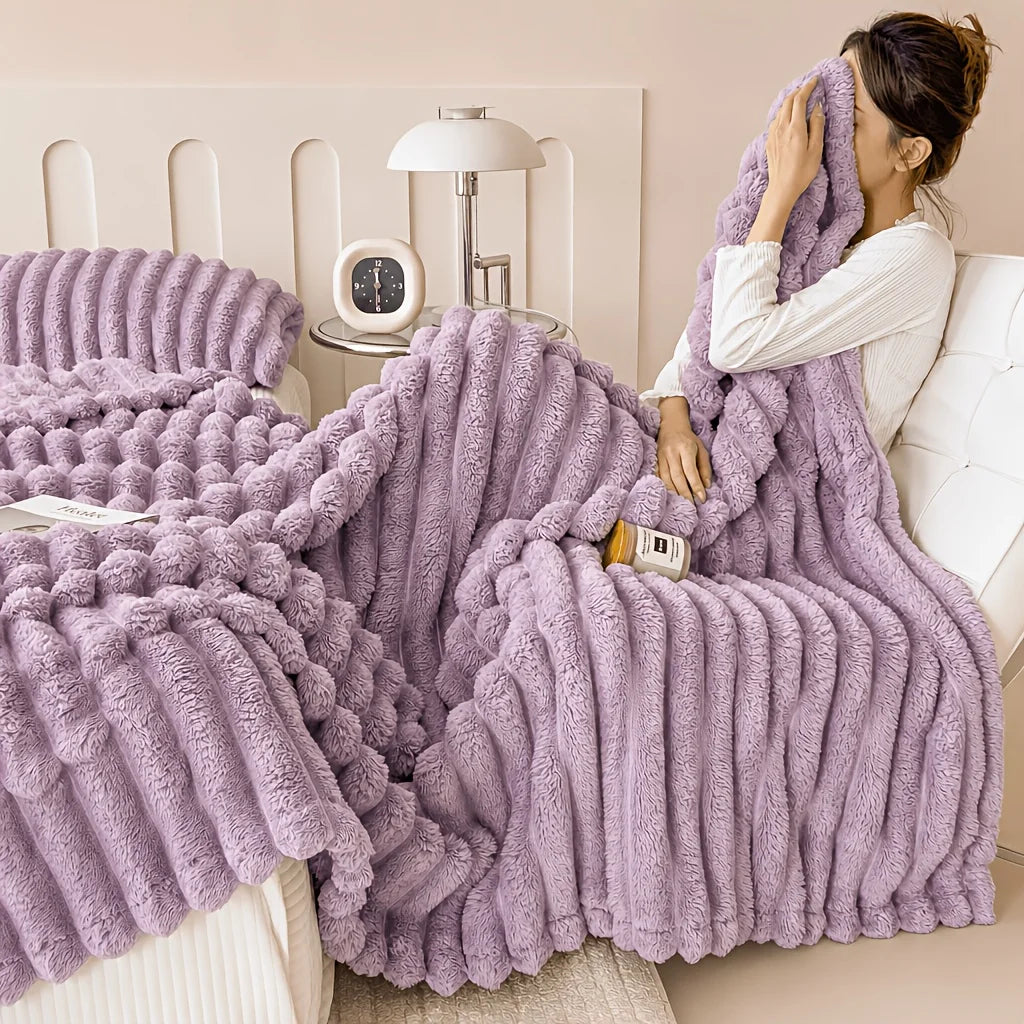 A fluffy purple fleece throw blanket draped over a white bed, being held by a person.