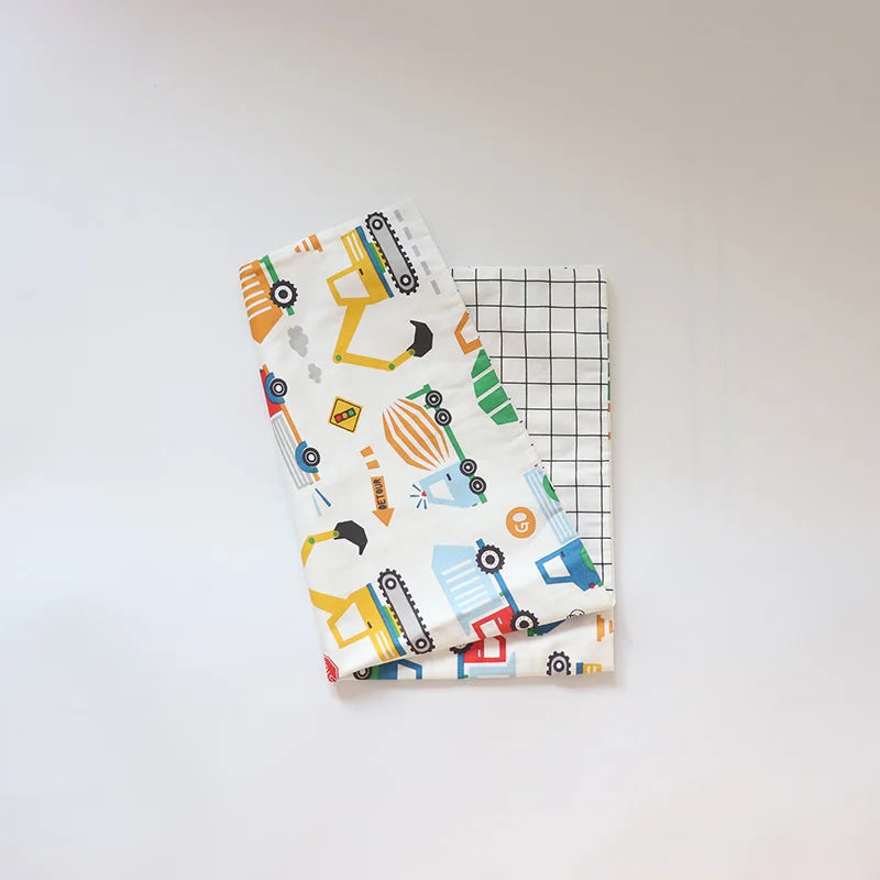 A white baby pillow cover featuring a colorful pattern of yellow and blue construction vehicles.