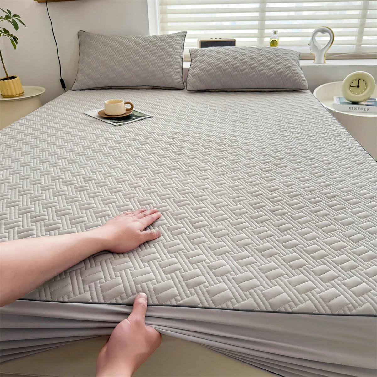 A close-up view of a gray cooling spandex fitted sheet mattress protector being touched on a bed.