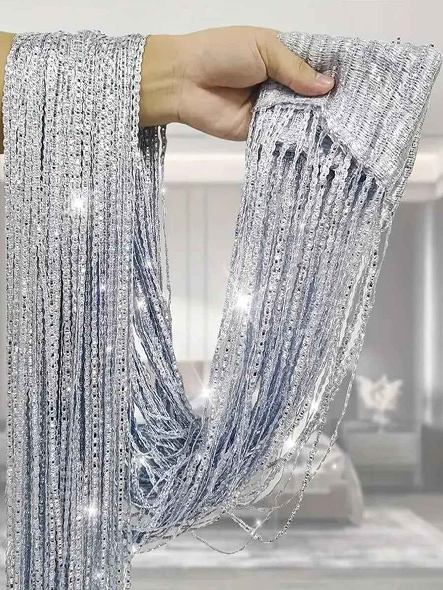 A hand holds a long, silver beaded string curtain with fringe details.
