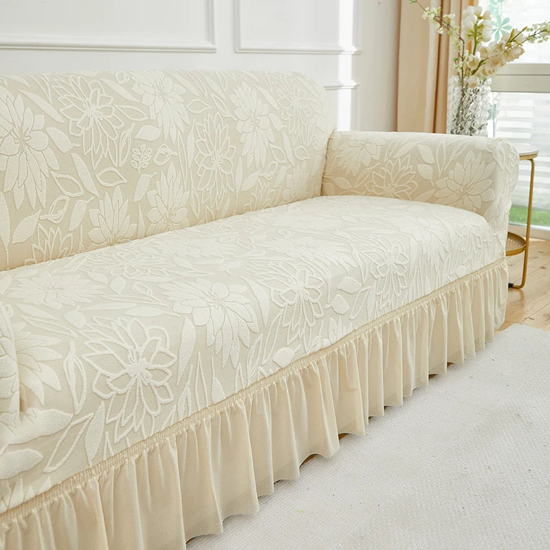 A cream-colored jacquard stretch sofa cover featuring a floral pattern and ruffled trim.
