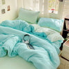 A light blue cotton bed linen set with matching pillows and a duvet cover displayed in a bright bedroom.