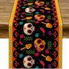 A vibrant Day of the Dead sugar skull linen table runner featuring colorful skulls and floral patterns on an orange backgroun
