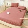 A red and white checkered fitted sheet is laid out on a bed, with pillows and decorative items nearby.