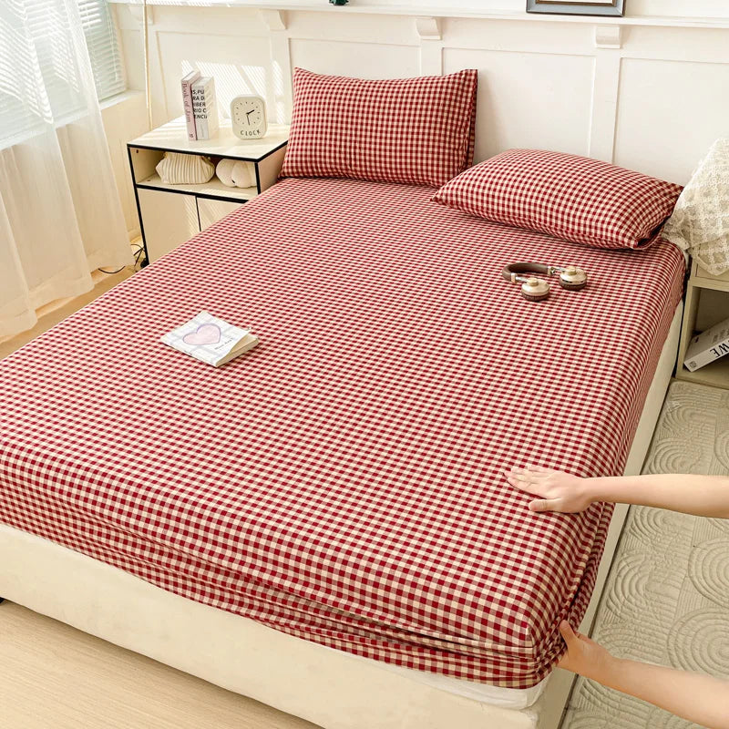 A red and white checkered fitted sheet is laid out on a bed, with pillows and decorative items nearby.
