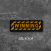 A black woven badge with the word WINNING in yellow text on a dark gray textured background.