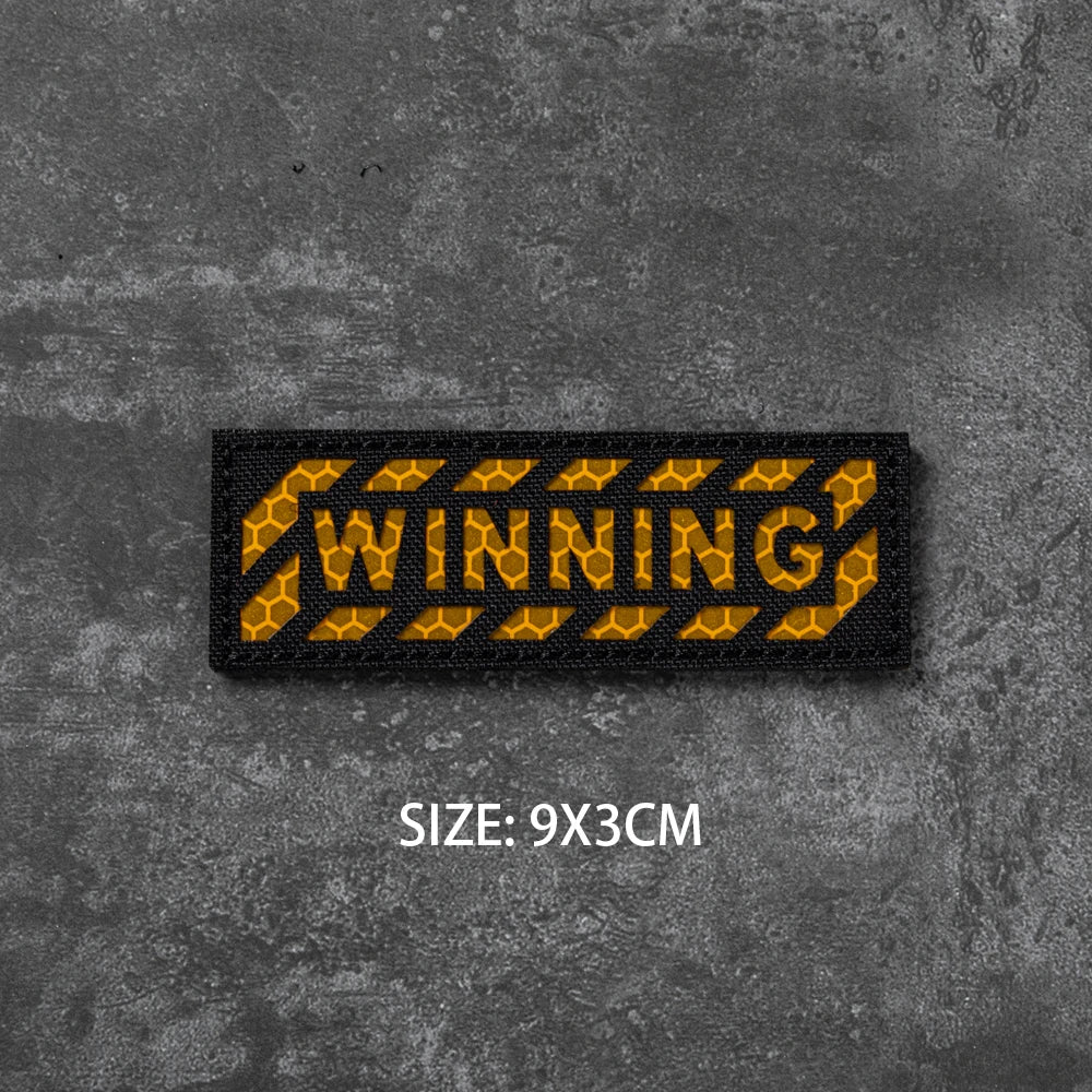 A black woven badge with the word WINNING in yellow text on a dark gray textured background.
