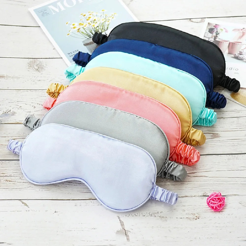 A collection of silk sleep masks in various pastel and dark colors laid out on a white wooden surface.