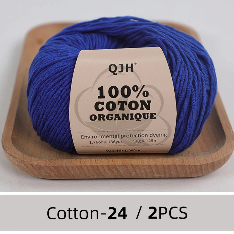 A ball of royal blue 100% organic cotton yarn labeled QJH for knitting and crochet placed on a wooden tray.