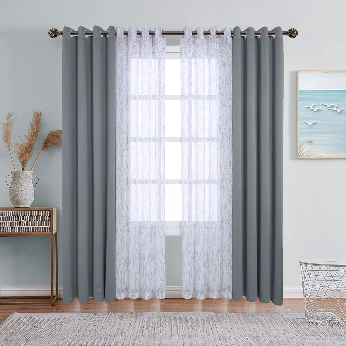 A set of gray and sheer white window drapes with grommets hanging on a rod.