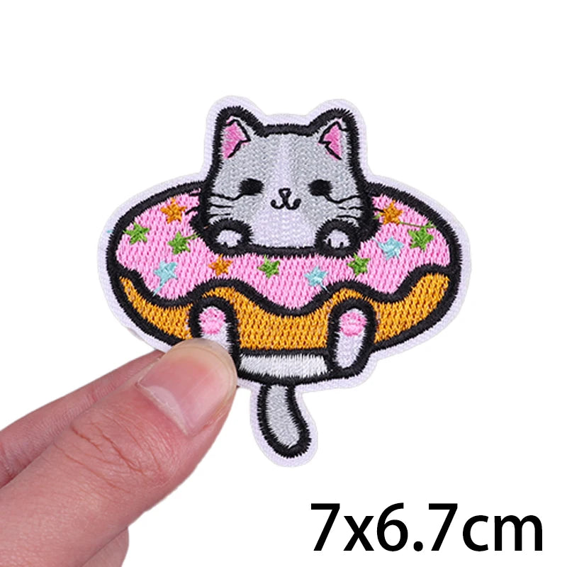 An embroidered iron-on patch featuring a cute black and white cat face surrounded by pink and green floral patterns.