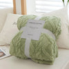 A light green plush double-sided throw blanket with a textured jacquard pattern is presented on a white surface.