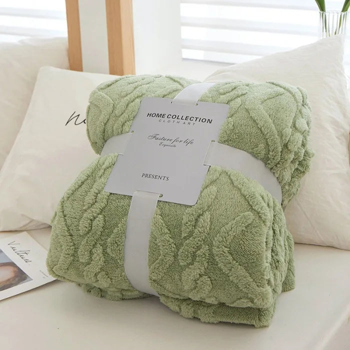 A light green plush double-sided throw blanket with a textured jacquard pattern is presented on a white surface.