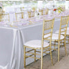 A long table set for a dining event with white satin tablecloths, gold chiavari chairs, and elegant place settings.