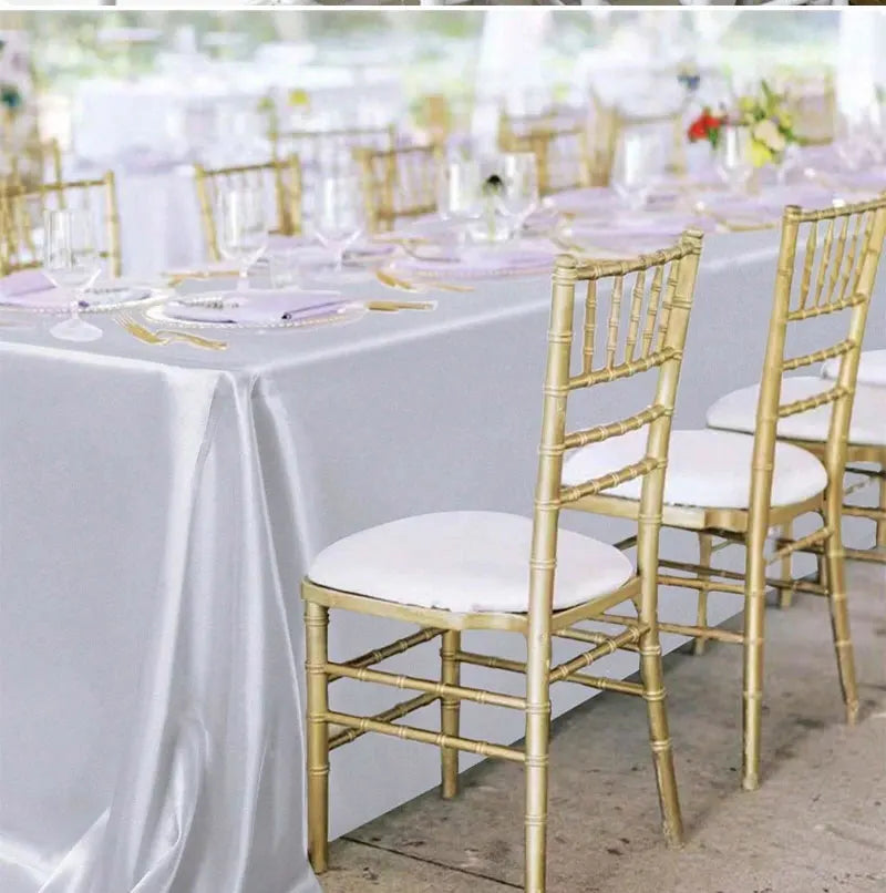 A long table set for a dining event with white satin tablecloths, gold chiavari chairs, and elegant place settings.