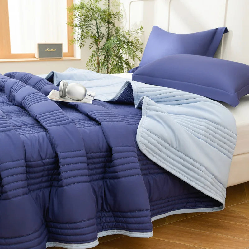 A navy blue quilted blanket is draped over a bed, with a light blue throw and purple pillows visible.