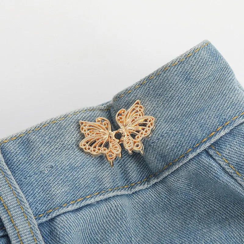A delicate gold-colored butterfly button clip is pinned onto a blue denim fabric.