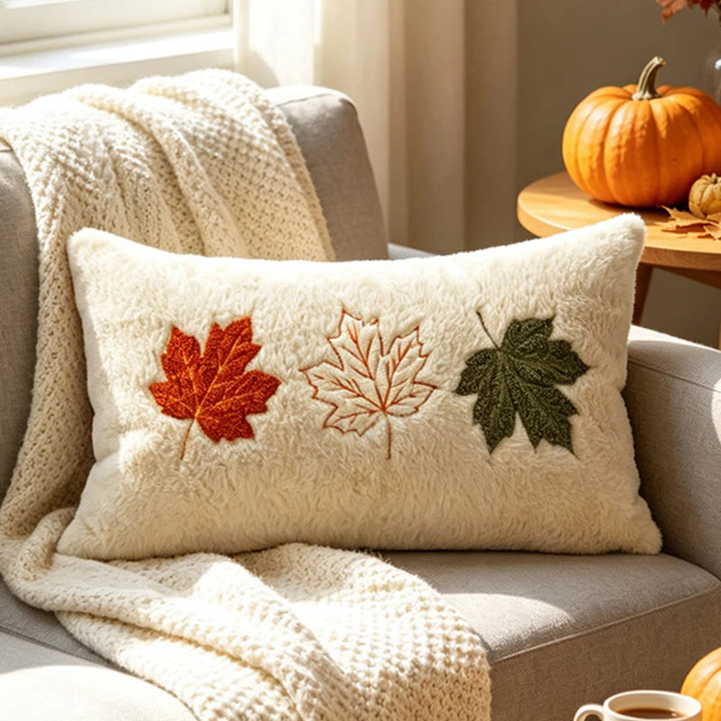 A cream-colored throw pillow featuring embroidered maple leaves in shades of orange, brown, and green.