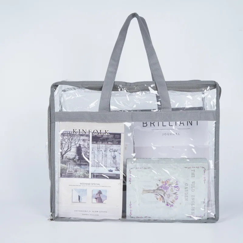 A gray fabric storage bag with a clear plastic window displaying a journal and other items.