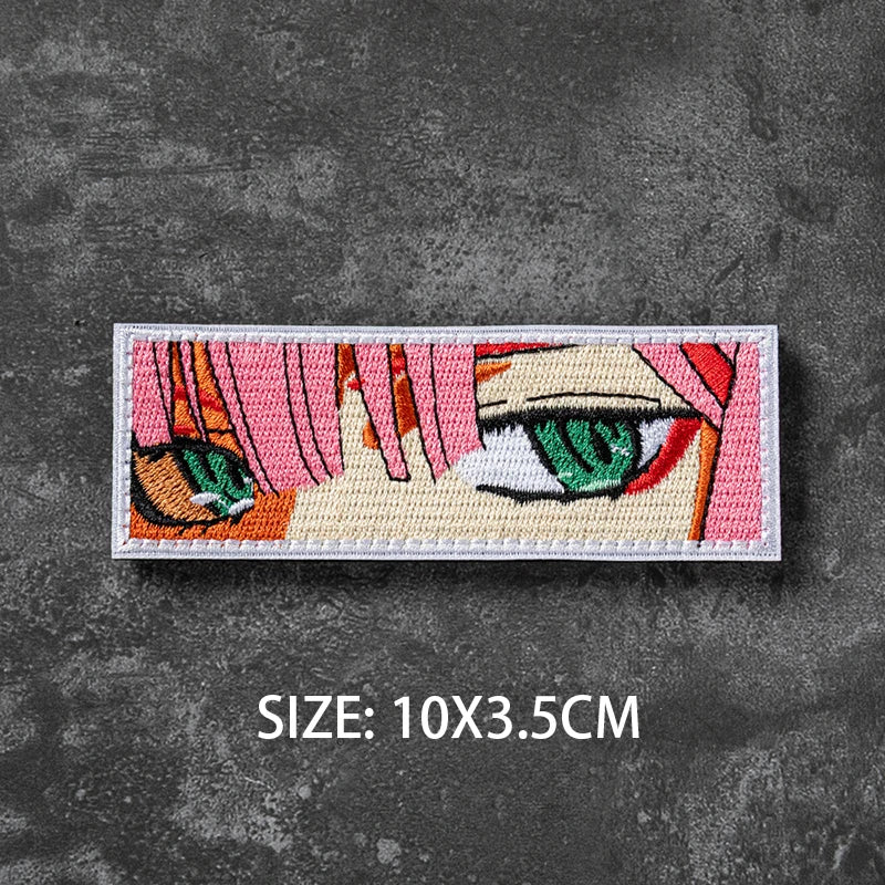 A square embroidered patch featuring a stylized female face with pink and orange hair and green eyes on a dark gray backgroun