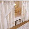 A white double-layer mesh bed canopy with lace trim hanging in a room.