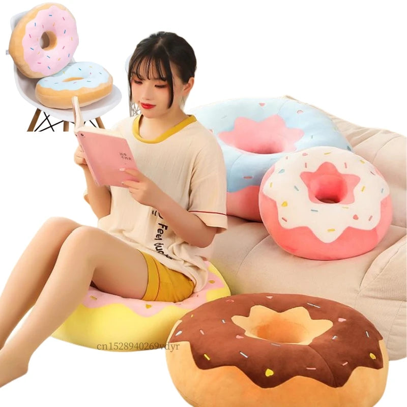 A young woman is sitting and holding a pink tablet while a large, round, pink and white donut plush pillow rests beside her.