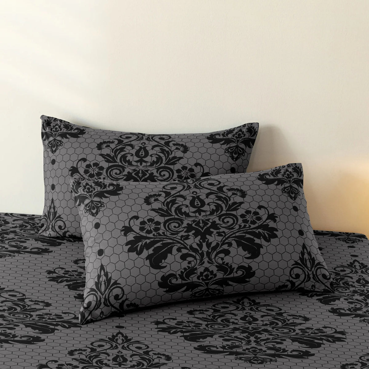 A black and gray damask pattern pillow resting on a matching duvet cover.