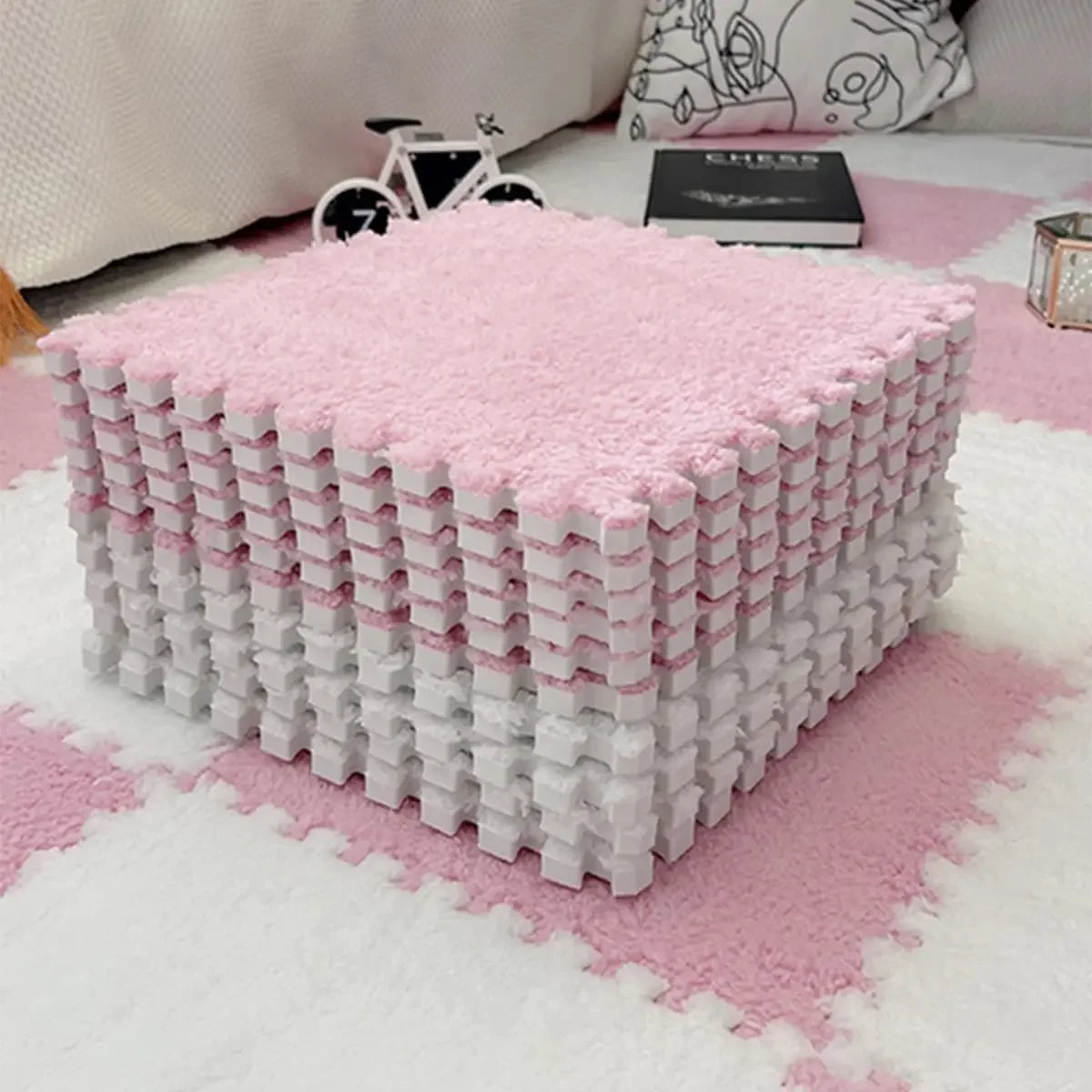 A large square play mat made of pink and white soft plush EVA foam tiles on a white rug.