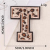A black iron-on patch shaped like the letter T with a leopard print design.