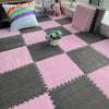 A pink and gray interlocking puzzle rug mat with a diamond pattern featuring a small vase of blue flowers and a plush toy.