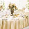 A close-up of a round table set for an event with gold satin overlays, white linens, and floral arrangements.