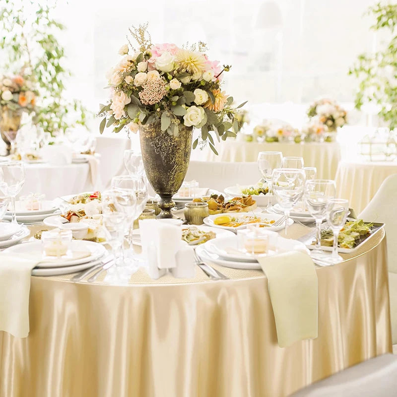 A close-up of a round table set for an event with gold satin overlays, white linens, and floral arrangements.