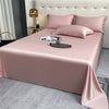 Pink luxury bamboo flat sheets spread on a bed with matching pillows and a bedside lamp.