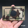 A rectangular tactical patch with a camouflage pattern and a circular black center is held in a hand.