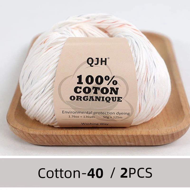 A ball of white organic cotton yarn labeled QJH 100% COTON ORGANIQUE resting on a wooden tray.