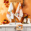A set of two kitchen towels with a pumpkin and plaid design hanging on a hook against an orange wall.