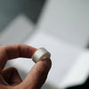 A hand holds a silver embroidery bobbin thread, showing the size and texture of the product.