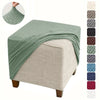 A green jacquard stretch ottoman slipcover draped over a beige upholstered ottoman.