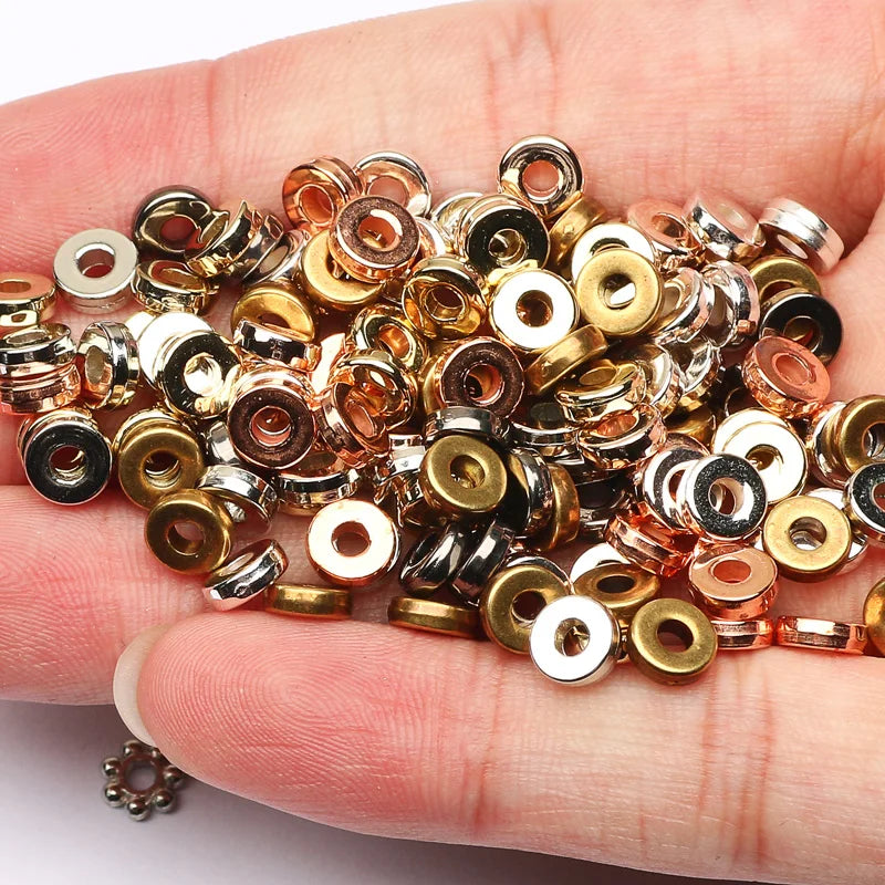 A hand holds a collection of small, round acrylic flat spacer beads in various gold and silver tones.
