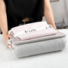 A hand is holding a stack of pink and gray bed sheet organizers with white straps on a white surface.