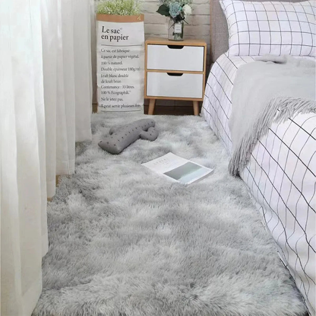 A fluffy gray silk wool floor rug placed in a bedroom setting next to a wooden cabinet and a white headboard.