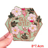 Pink letter embroidered iron-on patches featuring bees and wildflowers on a green fabric background