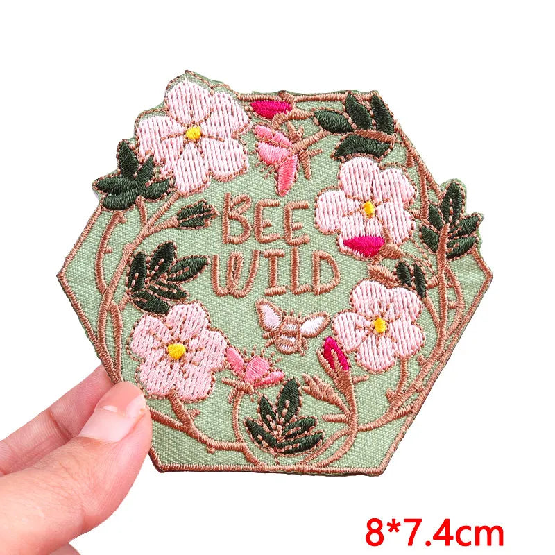 Pink letter embroidered iron-on patches featuring bees and wildflowers on a green fabric background